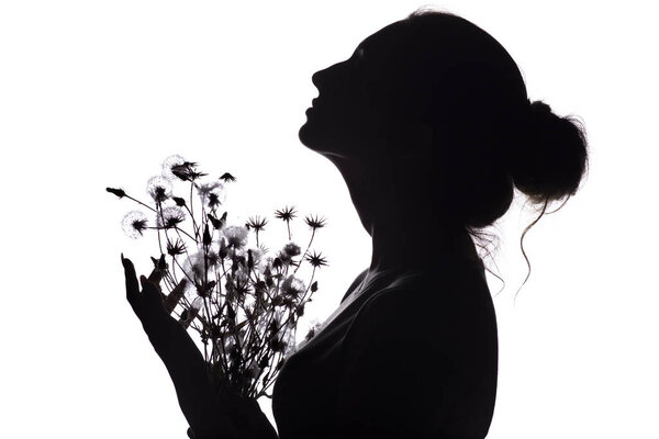 Silhouette of a beautiful girl with a bouquet of dried flowers, face profile of a dreamy young woman looking upwards on a white isolated background, the concept of beauty and femininity