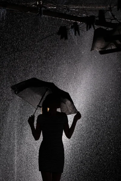 Silueta de la figura de una niña con un paraguas en la lluvia, un perfil de mujer joven —  Fotos de Stock