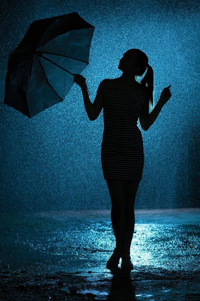 Silhouette della figura di una giovane ragazza con un ombrello sotto la pioggia, una giovane donna è felice di gocce d'acqua, concept meteo e umore — Foto Stock