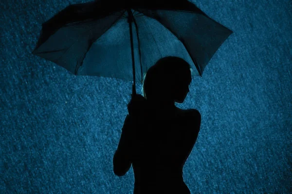 Silueta de la figura de una joven con un paraguas bajo la lluvia — Foto de Stock