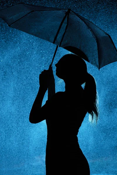 Silhouette della figura di una giovane ragazza con un ombrello sotto la pioggia, una giovane donna è felice di gocce d'acqua — Foto Stock