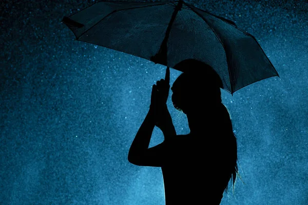 Silueta de la figura de una niña con un paraguas en la lluvia, una mujer joven está feliz de gotas de agua, el clima concepto y el estado de ánimo —  Fotos de Stock