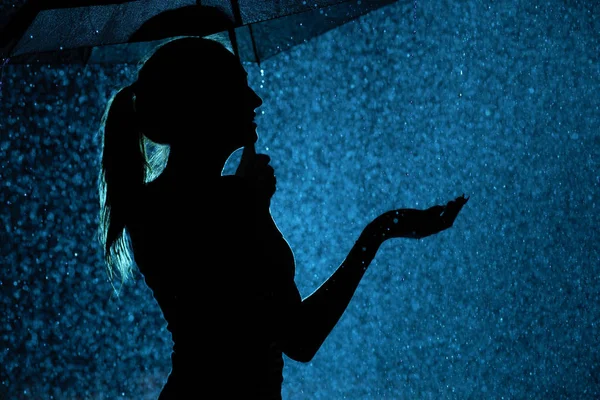 Silhouette della figura di una giovane ragazza con un ombrello sotto la pioggia, una giovane donna felice di gocce d'acqua — Foto Stock