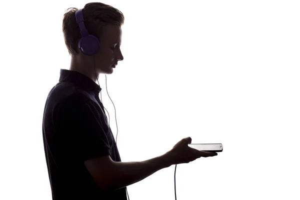 Silhouette de jeune homme écoutant de la musique dans les écouteurs, gars allumé votre musique préférée et profiter sur un fond blanc isolé — Photo