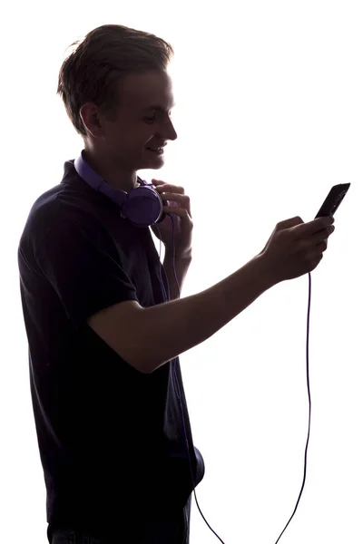 Silhouette d'un profil de jeune homme avec des écouteurs sur son cou et mp3 jouer dans les mains, adolescent garçon retourne à travers une playlist de musique sur un fond blanc isolé, concept mode de vie des jeunes — Photo