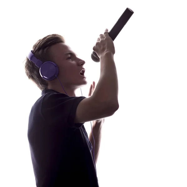 Silhouette de jeune homme dans les écouteurs chantant dans le microphone sur fond blanc isolé — Photo