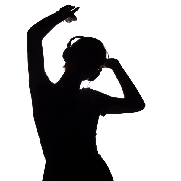 Silhouet van een gelukkig meisje luisteren naar muziek in een koptelefoon, figuur van jonge vrouw met handen omhoog ontspannen op een witte geïsoleerde achtergrond en dansen op de muziek — Stockfoto