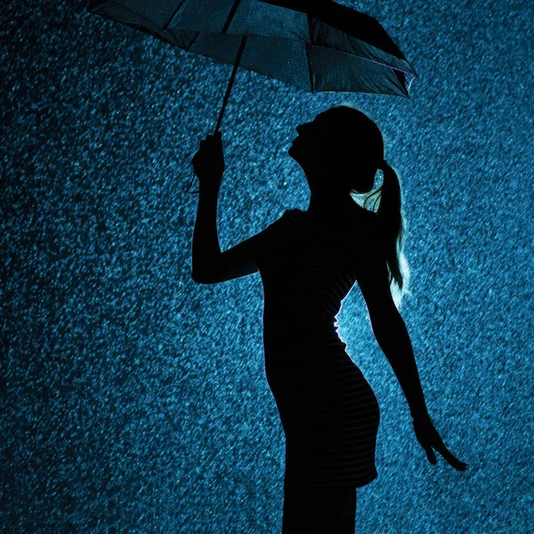 Silhouette della figura di una giovane ragazza con un ombrello sotto la pioggia, una giovane donna con i capelli raccolti a mano è felice di gocce d'acqua, concept meteo e umore — Foto Stock