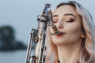 Doğadaki genç müzisyen portresi, saksafon çalan ve trompete üfleyen kadın yüzü, konsept müzik ve rahatlama.