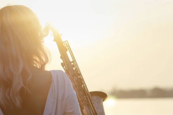 Silhouette d'une jeune belle jeune fille jouant du saxophone au lever du soleil au bord de la rivière, femme sur la nature au lever du soleil donnant un concert et relaxant, concept music — Photo