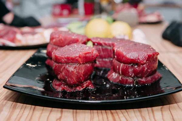 Raw beef meat for steak preparation. Raw beef sliced, preparation of meat for cooking steak at the culinary master class. Raw meat on a black plate.