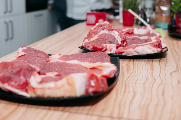 Raw beef meat for steak preparation. Raw beef sliced, preparation of meat for cooking steak at the culinary master class. Raw meat on a black plate.
