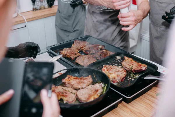 cooking steaks in a pan. cooking beef at the culinary master class. the hands of the chef in black gloves.