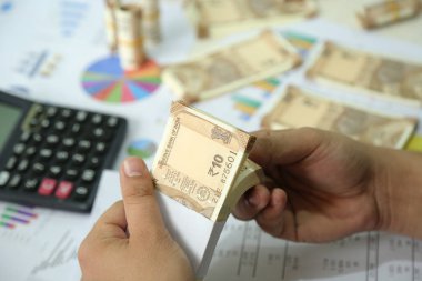 Adam elinde 10 rupilik hint para notu tutuyor. Hesap makinesi, grafik kağıdı, Hint para birimi notları resmi.