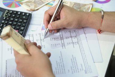 Adam kalemle hesabı kontrol ediyor ve elinde Hint para notları tutuyor..