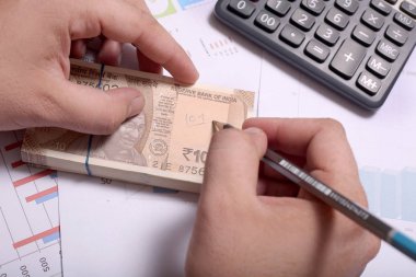 Adam elinde Hint para notu ve kalem tutan bir hesap makinesi kullanıyor.