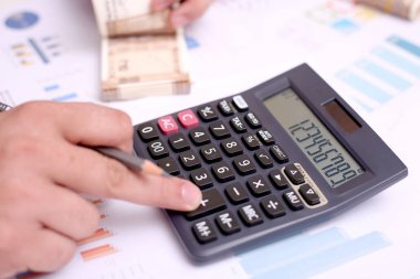 Adam elinde bir kalem ve yeni Hint notları tutan bir hesap makinesi kullanıyor.