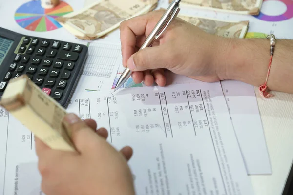 Adam kalemle hesabı kontrol ediyor ve elinde Hint para notları tutuyor..