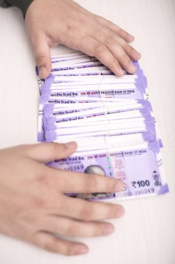 Adam masada 100 rupi yeni Hint parası gösteriyor. Ahşap arka planda izole.