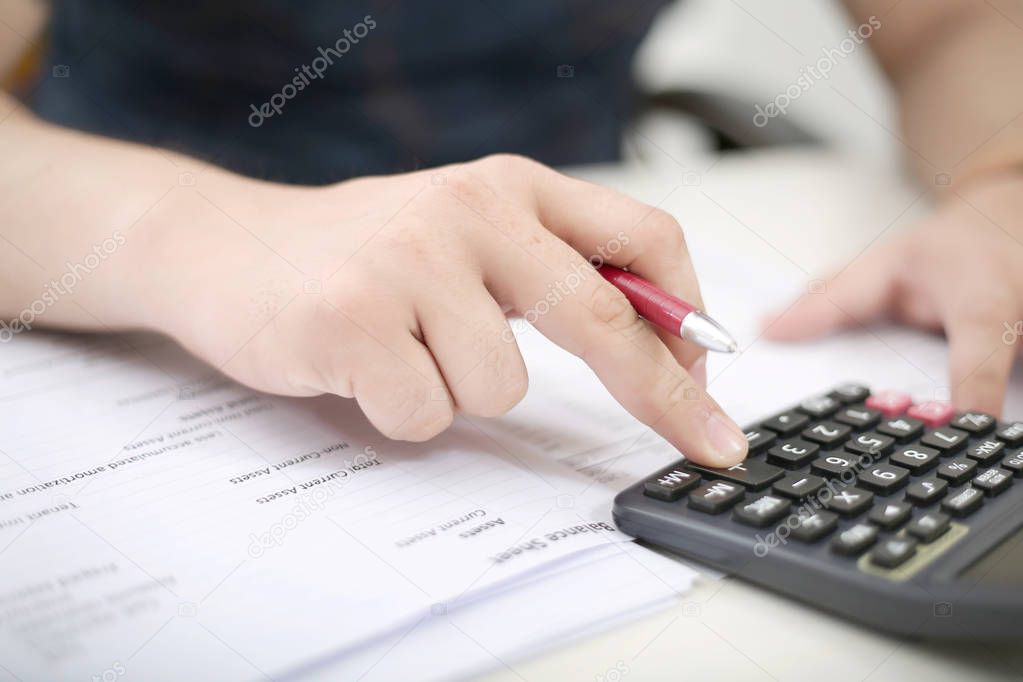 Man is using a calculator with holding a pen in hand.