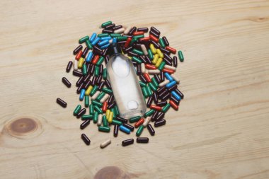 Ahşap arka planda izole edilmiş birden fazla kapsül. Haplar herhangi bir ilaç, bitkisel veya kimyasal içerebilir. Ürün paketleme tıbbı için kullanılan beyaz şişe.