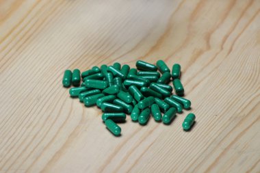 Ahşap arka planda yeşil vitamin kapsülü. 
