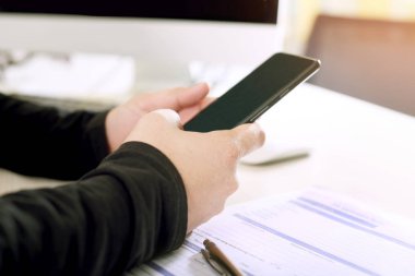 Bir işadamı masaüstünde çalışırken formu ile bir telefon kullanıyor.