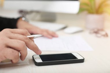 Adam masaüstünde çalışırken telefon kullanıyor.