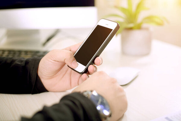 A young man is Using a phone with one hand while working on a desktop.