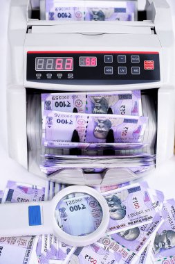 Yeni 100 rupilik banknotlar ve büyüteçile para sayma makinesi. Beyaz arka planda yalıtılmış.