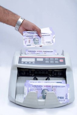 Adam eli nakit sayma makinesine yeni 100 rupilik banknotlar koyuyor. Beyaz arka planda yalıtılmış.