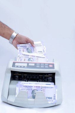 Adam el portresi nakit sayma makinesine yeni 100 rupilik banknotlar koyuyor. Beyaz arka planda yalıtılmış.