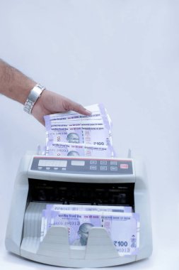 Adam el resmi nakit sayma makinesinde yeni Hint 100 rupi para koyarak. Beyaz arka planda yalıtılmış.