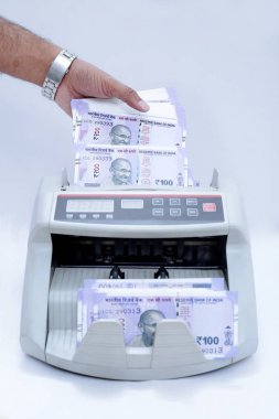 Adam elresmi nakit sayma makinesine yeni 100 rupilik banknotlar koyuyor. Beyaz arka planda yalıtılmış.