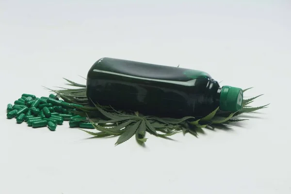 大麻叶装饰下阿育吠陀药绿色瓶 在白色背景上隔离的阿育吠陀绿色片剂 — 图库照片