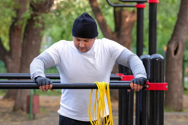 Street workout of a young man in the early Sunny morning. The man is preparing to perform a power load on the simulator and rubs sports magnesia.