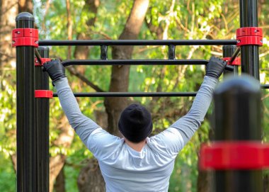 Genç bir adam simülatör crossbar çekerek bir spor egzersiz icra. Açık hava eğitimi sırt kasları, deltoidler, triceps ve pazı gücünü geliştirir.