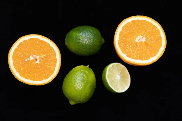 Tropical fruits orange and lime in whole form and sliced on black background.