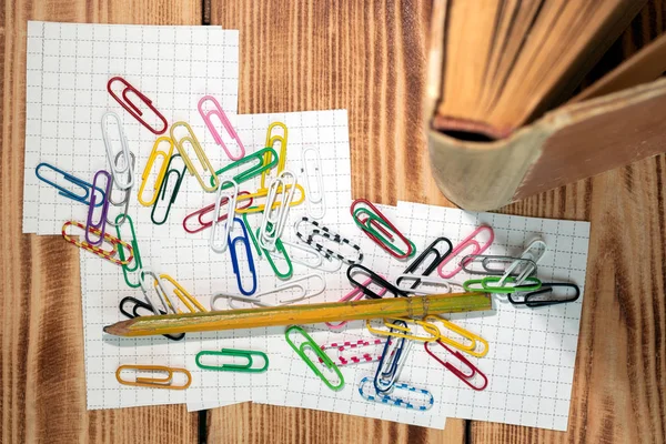 Colored clips for labeling tabs while studying at the mess of scattered on pieces of paper for notes. Old scribbled pencil thrown on top of the mess