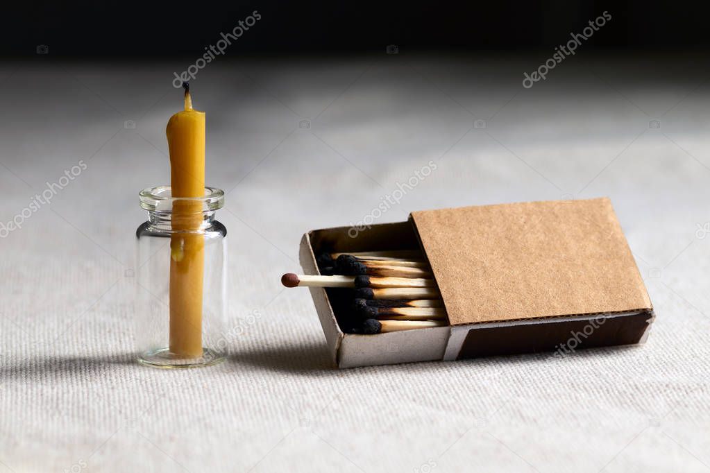 In a dark room on the table is an extinct candle. One single working match among the burned sticking out of the box symbolizes a chance for revival and development.
