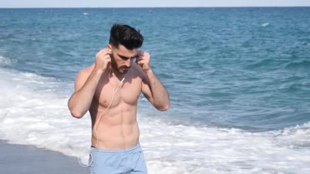 Jeune homme à la plage écoutant de la musique avec des écouteurs — Video