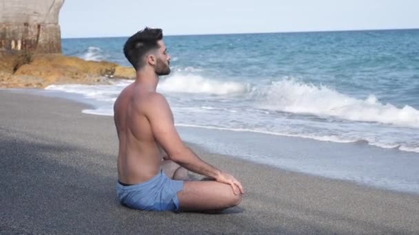 Hombre joven meditando o haciendo ejercicio de yoga por el mar — Vídeo de stock