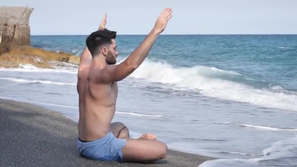 Jonge man mediteren of het doen van yoga oefening door zee — Stockvideo