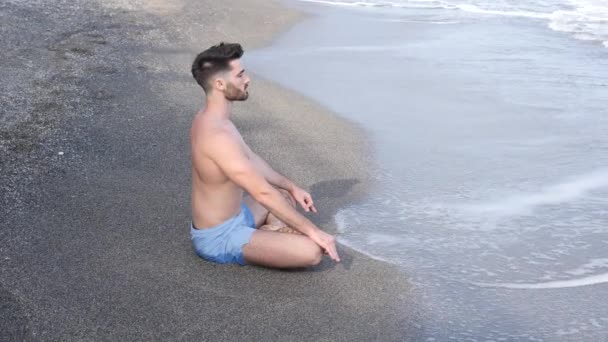 Jonge man mediteren of het doen van yoga oefening door zee — Stockvideo