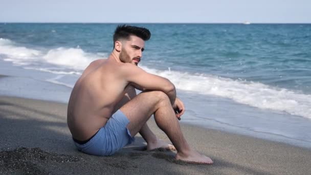 Jovem sentado numa praia sozinho e solitário — Vídeo de Stock