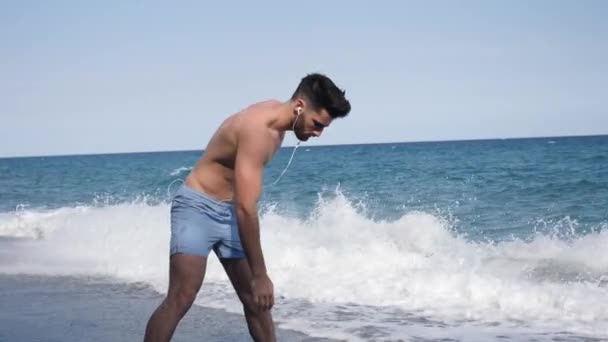 Jeune homme faisant des exercices d'étirement sur la plage — Video