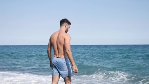Молодой человек, гуляющий по пляжу один — стоковое видео