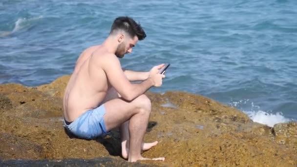 Joven en el mar leyendo con lector de libros electrónicos — Vídeos de Stock