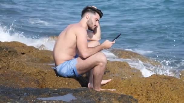 Joven en el mar leyendo con lector de libros electrónicos — Vídeo de stock