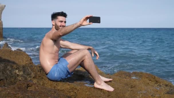 Jonge man op strand met behulp van de mobiele telefoon naar de film van de zee — Stockvideo